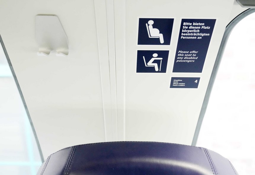 Das Foto zeigt Piktogramme über einem Sitzplatz, die darauf hinweisen, dass es sich um einen Platz für mobilitätseingeschränkte Fahrgäste handelt.