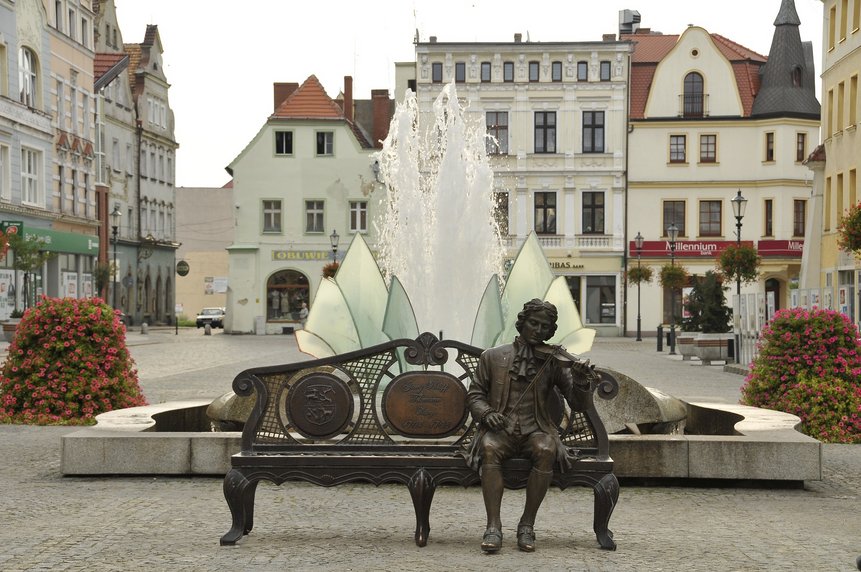 Georg-Philipp-Telemann-Denkmal am Marktplatz in Żary. Im Hintergrund ist sind ein Springbrunnen sowie Wohnhäuser zu sehen.