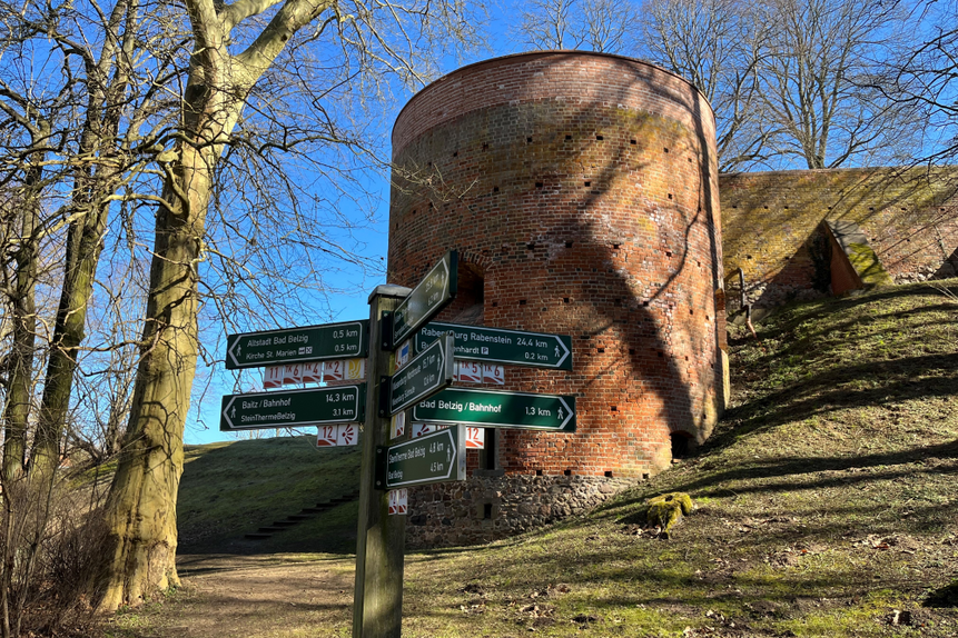 Das Foto zeigt Wander-Wegweiser und im Hintergrund einen Burgturm.