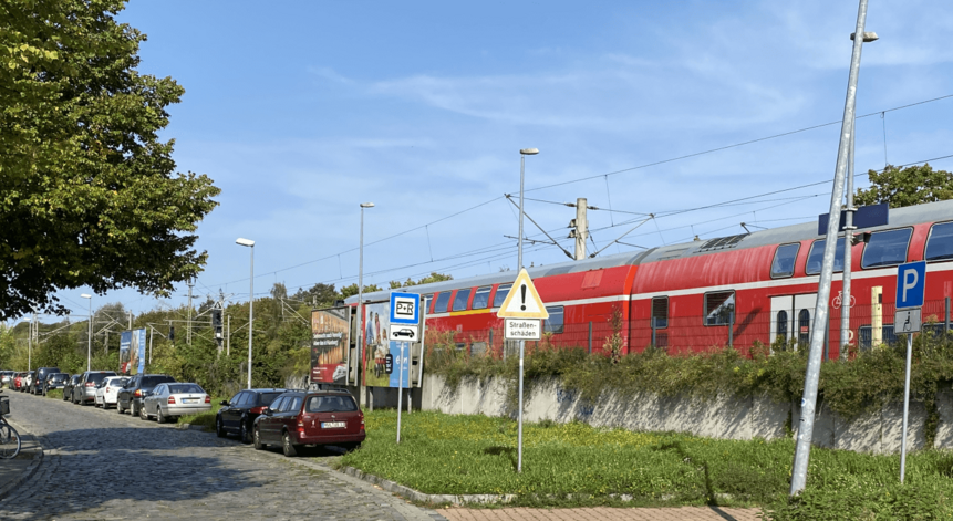 Autos auf dem Parkplatz am Bahnhof Falkensee. Im Hintergrund ein Zug.