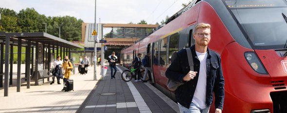 Junger Mann vor DB Regionalbahn am Bahnhof Struveshof