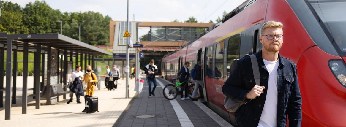 Junger Mann vor DB Regionalbahn am Bahnhof Struveshof