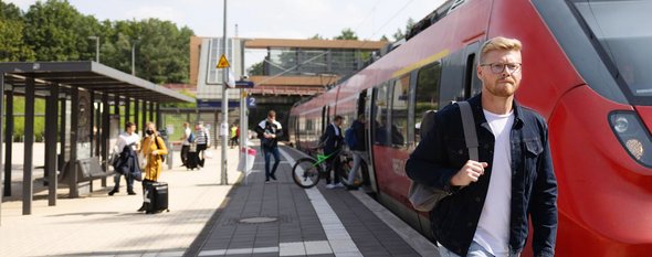 Junger Mann vor DB Regionalbahn am Bahnhof Struveshof