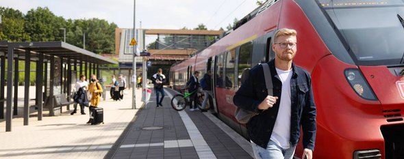 Junger Mann vor DB Regionalbahn am Bahnhof Struveshof