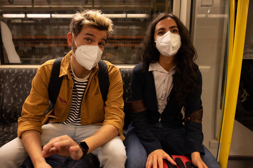 Ein Mann und eine Frau sitzen in der U-Bahn und tragen eine FFP2-Maske