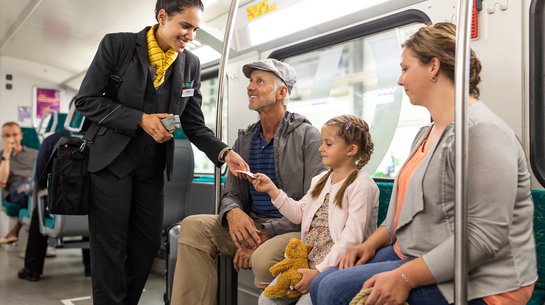 Das Foto zeigt eine Kundenbetreuerin, die im Zug gerade Fahrscheine einer Familie kontrolliert.