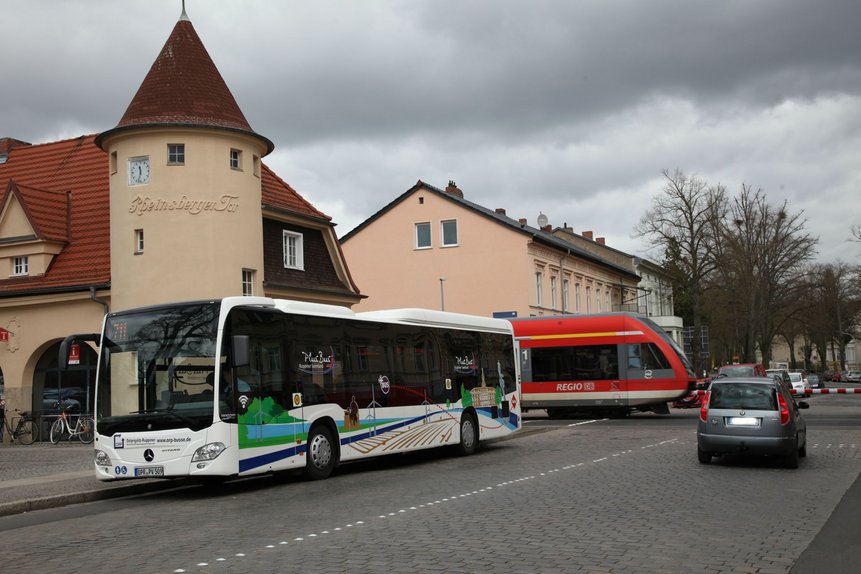 Der PlusBUs der Linie 711 steht an einer Haltestelle. Im Hintergrund fährt ein Regionalexpress