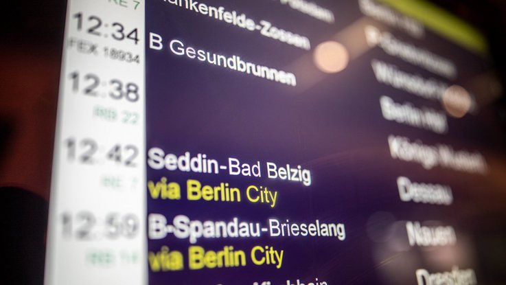 Das Bild zeigt einen Abfahrtsmonitor in einem Bahnhof mit Abfahrten von Zügen.