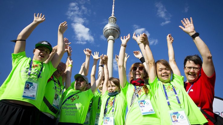 Teilnehmer*innen der Weltspiele strecken die Hände in die Höhe. Im Hintergrund der Berliner Fernsehturm.