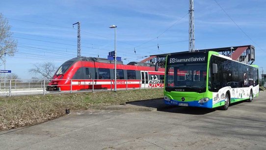 Das Foto zeigt einen Zug und einen Bus nebeneinander am Bahnhof Saarmund.