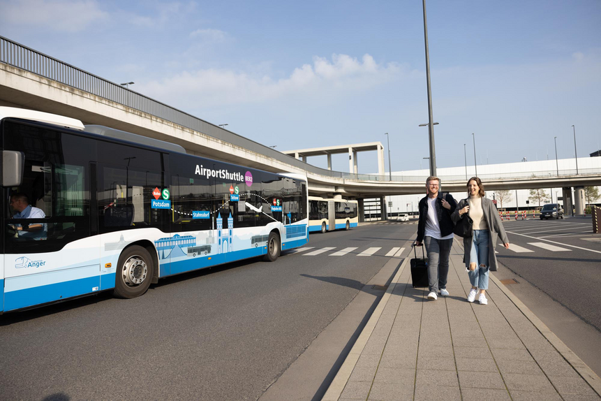 AirportShuttle-Bus BER2 Das Foto zeigt zwei Personen mit Gepäck vor dem Eingang des Flughafens BER.