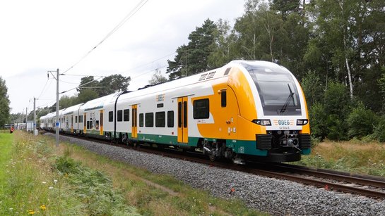 Das Foto zeigt den Desiro HC-Zug von außen auf einer Bahnstrecke durch die Natur.