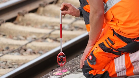 Blick auf einen Bauarbeiter der DB, der an den Schienen kniet und arbeitet