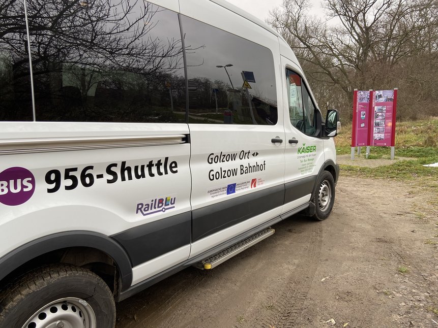 Seitenansicht eines Shuttlebusses mit der Beklebung (Busliniennummer 956-Shuttle, Relation: Golzow Ort - Golzow Bahnhof, RailBLu- und EU-Logo