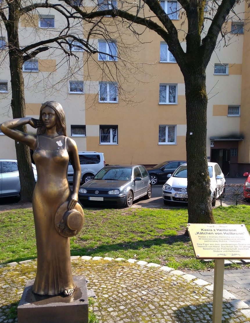 Figur Käthchen von Heilbronn. Im Hintergrund ein Parkplatz sowie ein gelber Wohnblock.