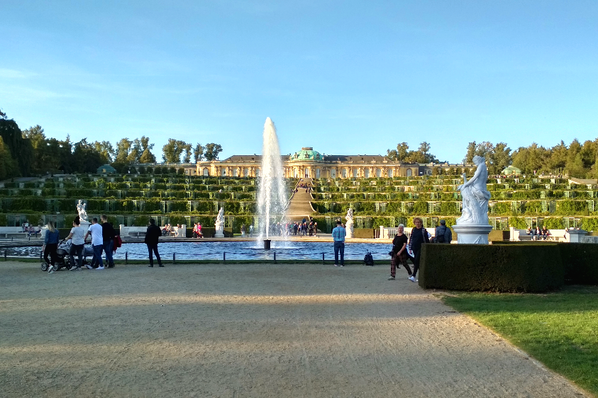 Das Foto zeigt eine Wasserfontäne, im Hintergrund das Schloss Sanssouci in Potsdam