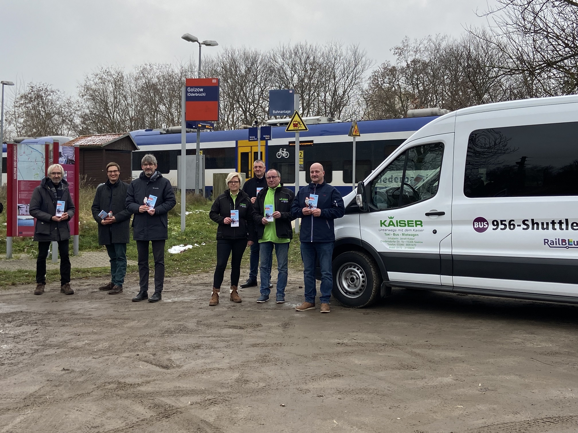 Shuttlebus direkt vor dem Bahnsteig mit dem Zug der Linie RB26 im Hintergrund. Links neben dem Bus stehen Jürgen-Peter Hiller vom Ministerium für Infrastruktur und Landesplanung, Max Goethel vom VBB, Golzows Bürgermeister Frank Schütz, Busunternehmerin Janett Kaiser, Torsten Heisler von der mobus Märkisch-Oderland Bus GmbH, Dietmar Kaiser vom Busunternehmen Kaiser und Heiko Arndt von der mobus Märkisch-Oderland Bus GmbH.